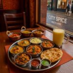 A colourful Indian thali buffet at City Spice in London, featuring Bengali dishes like chicken rezala, shatkora dal, and chana masala with naan and chutneys.